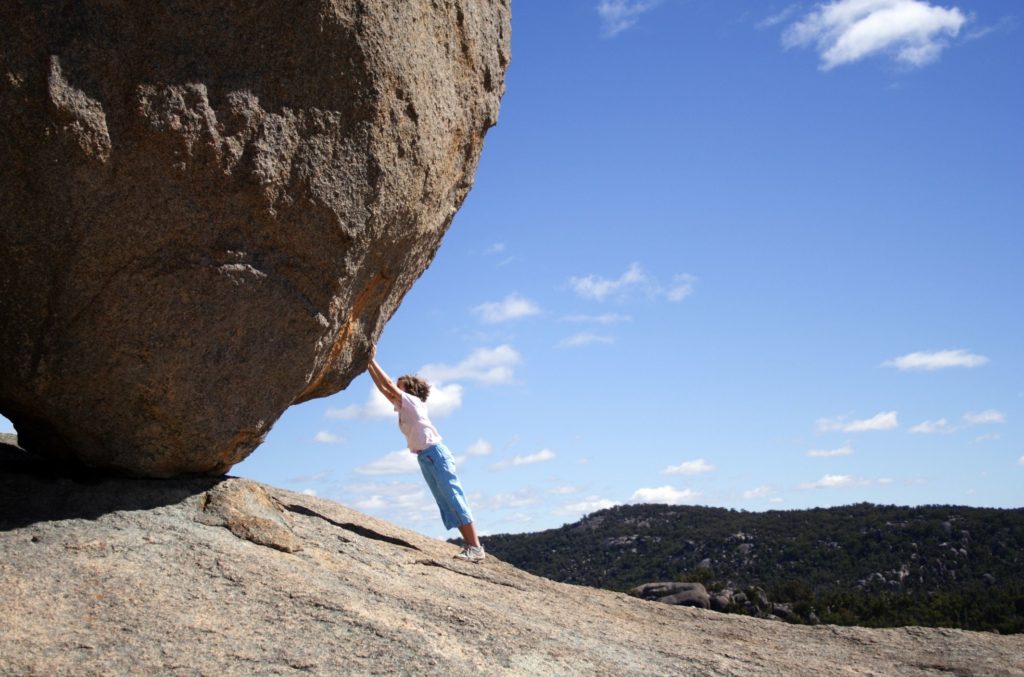 woman pushing boulder representing catastrophic anxious thinking