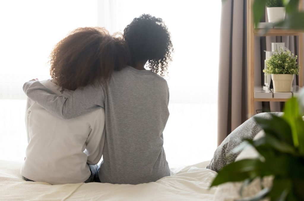black women on bed support each other to cope with racial battle fatigue and racial trauma