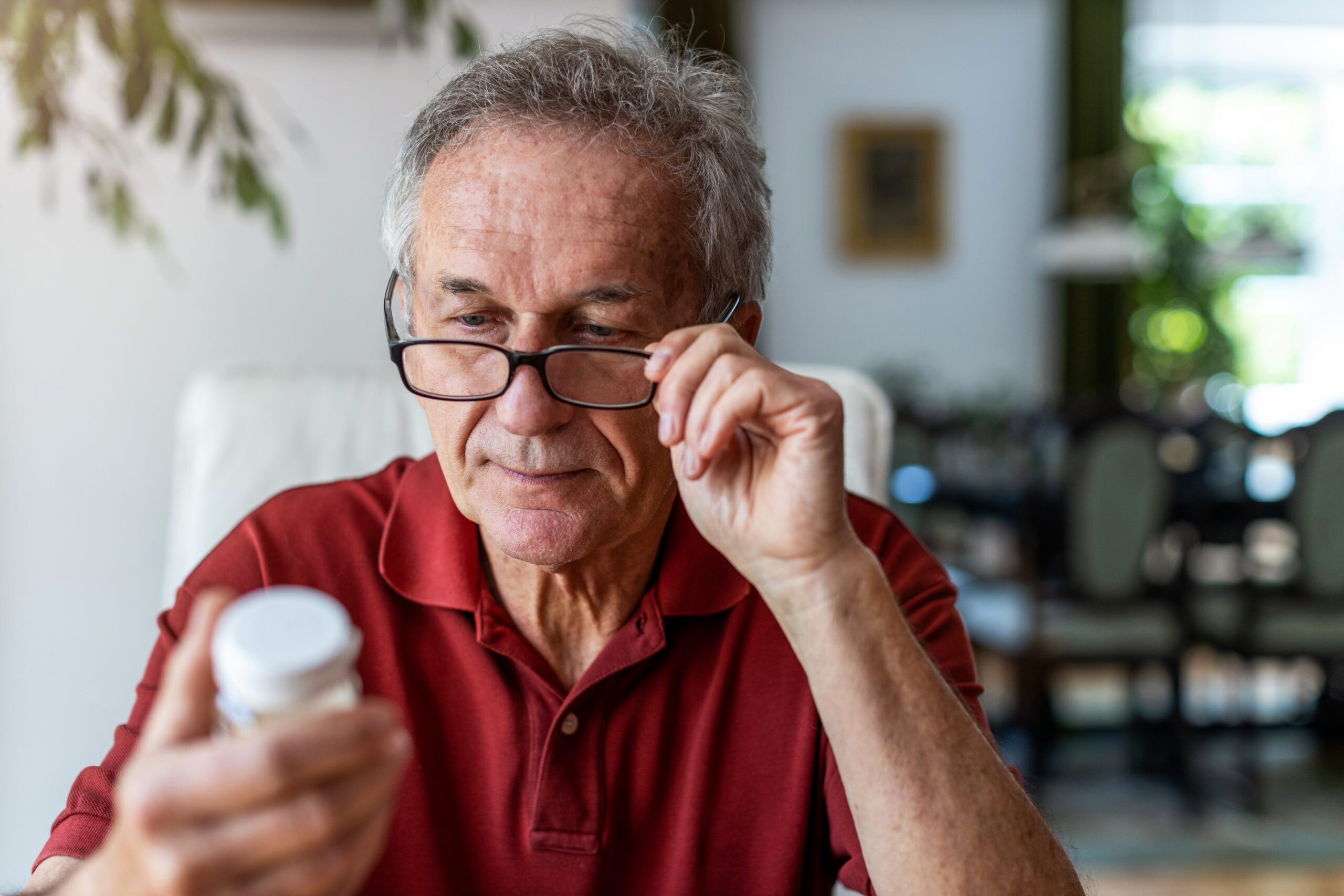 Older man examining a medication bottle closely, evaluating the different prescription dosages for erectile dysfunction treatments.