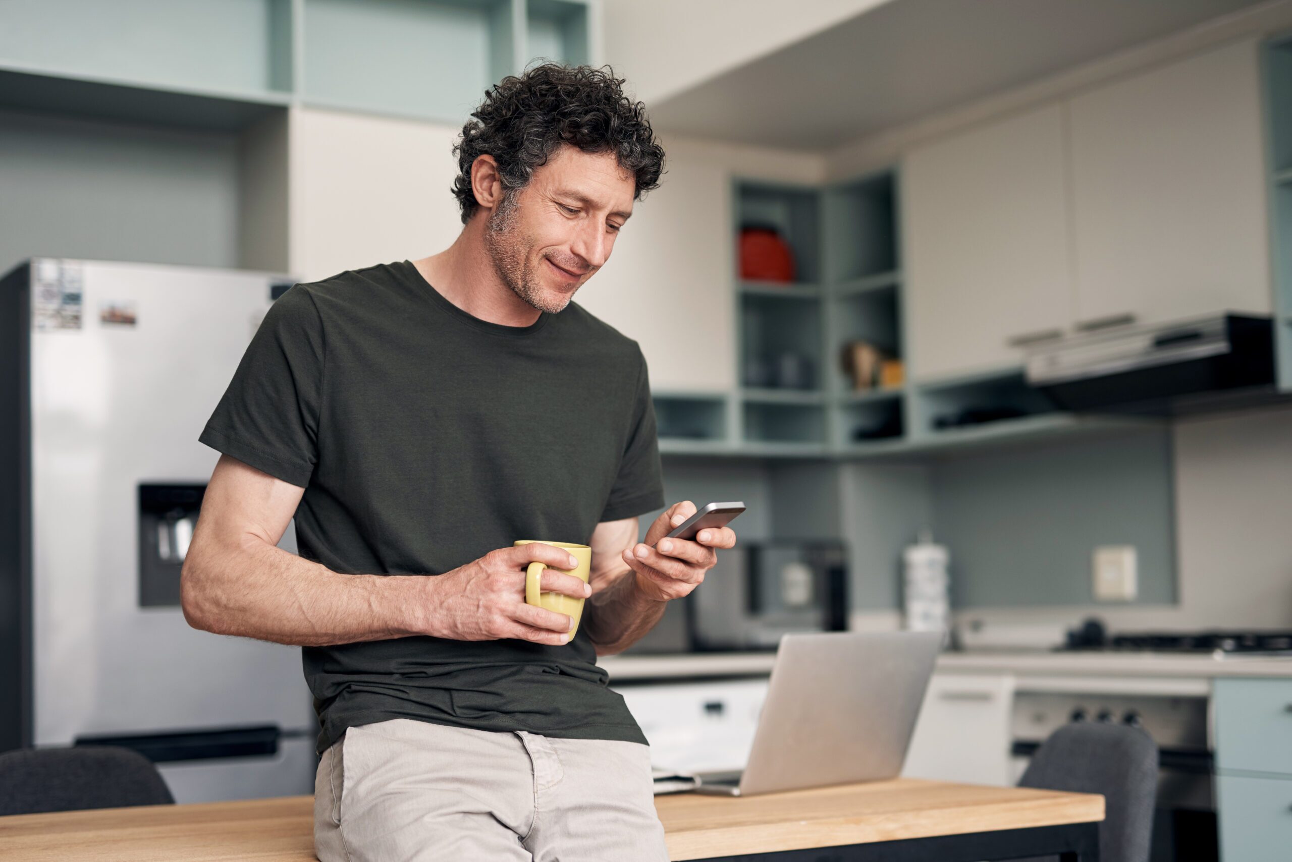 Man reading a smartphone while holding a cup of coffee, considering the risks of drinking alcohol while taking Zoloft® and its potential effects on health.